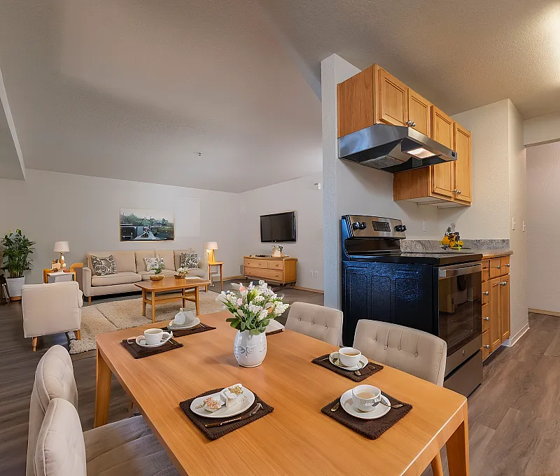 Inviting open-plan apartment interior featuring a cozy living room, a stylish dining area with seating for four, modern kitchen appliances, and elegant wooden cabinetry.