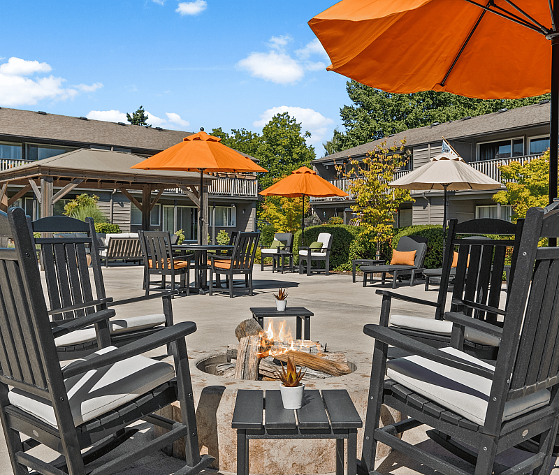 Charming courtyard with cozy seating, orange umbrellas, and a warm fire pit, offering a welcoming outdoor retreat.