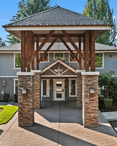 Inviting apartment building entrance with elegant stone pillars, lush greenery, and a modern architectural design.