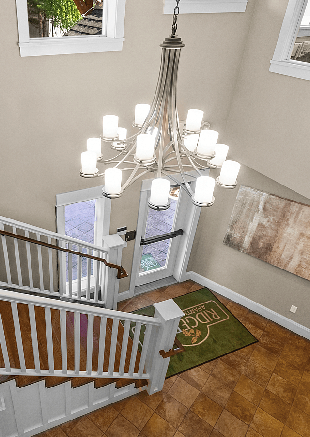 Elegant apartment lobby with a grand chandelier, modern artwork, and a stylish wooden staircase welcoming guests.