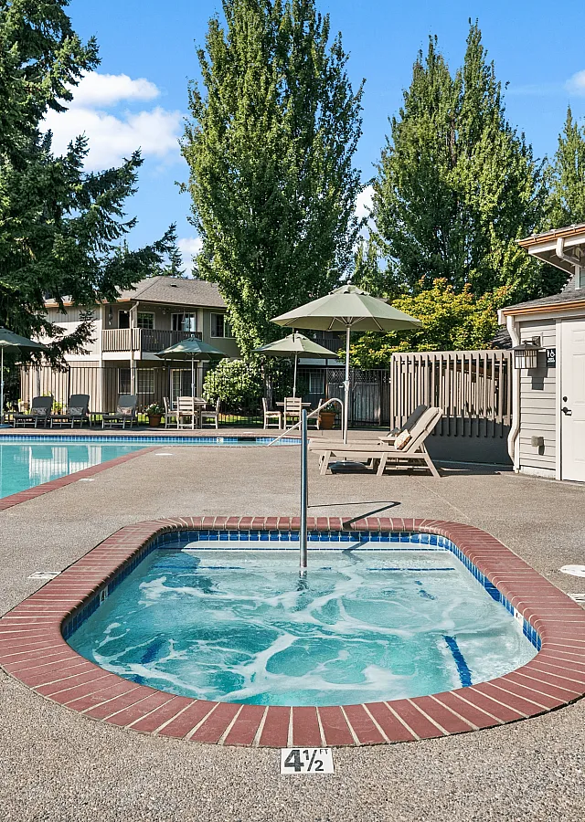 Inviting outdoor space with a sparkling pool and relaxing hot tub, surrounded by lush greenery and comfortable seating under umbrellas.