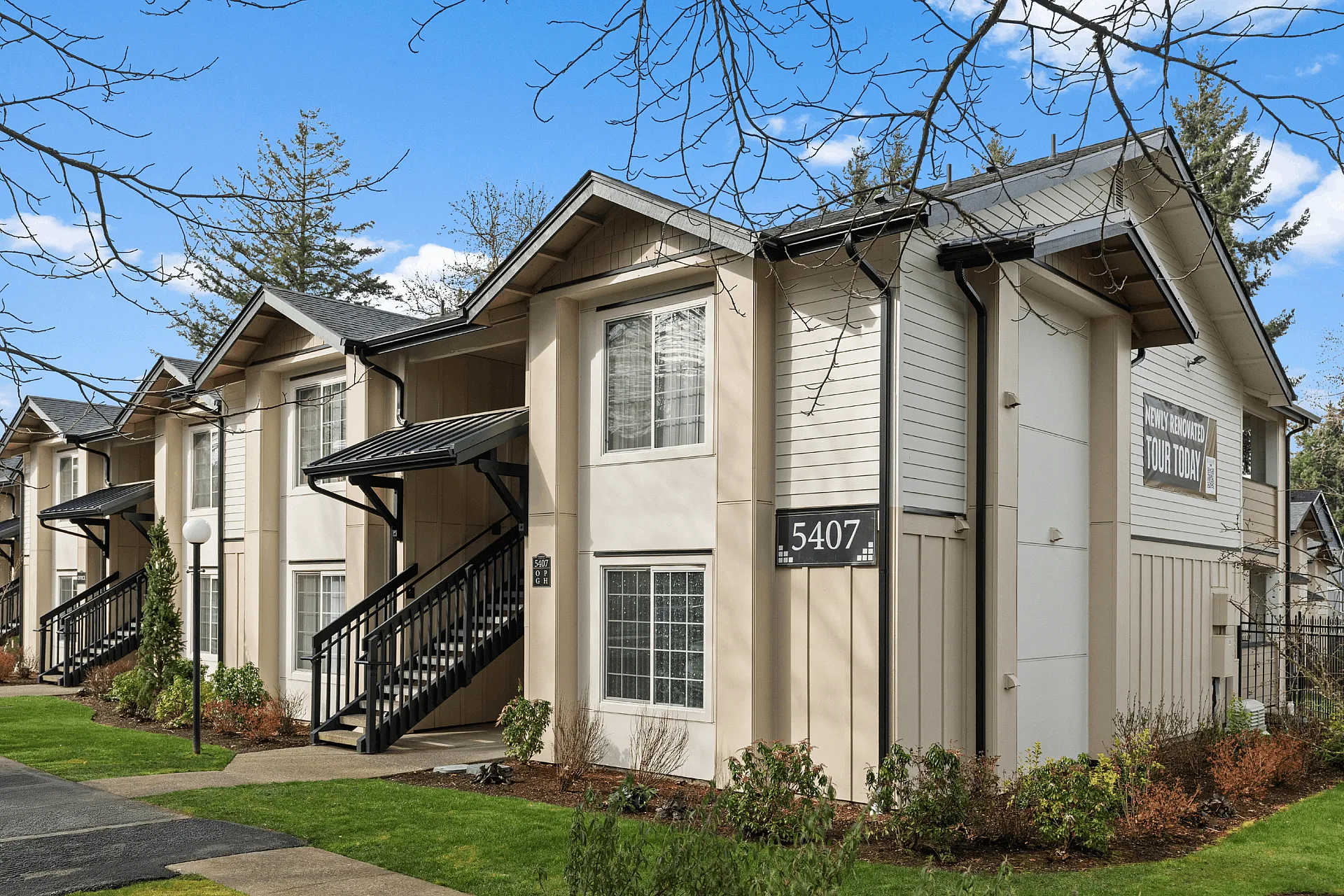 Charming apartment complex with modern exterior, featuring inviting paths, lush green lawns, and stairways leading to each unit.