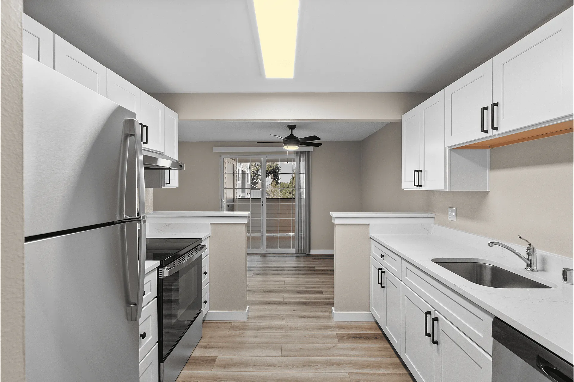 Modern kitchen with sleek stainless steel appliances, elegant white cabinetry, and warm hardwood flooring leading to a bright, inviting patio view.