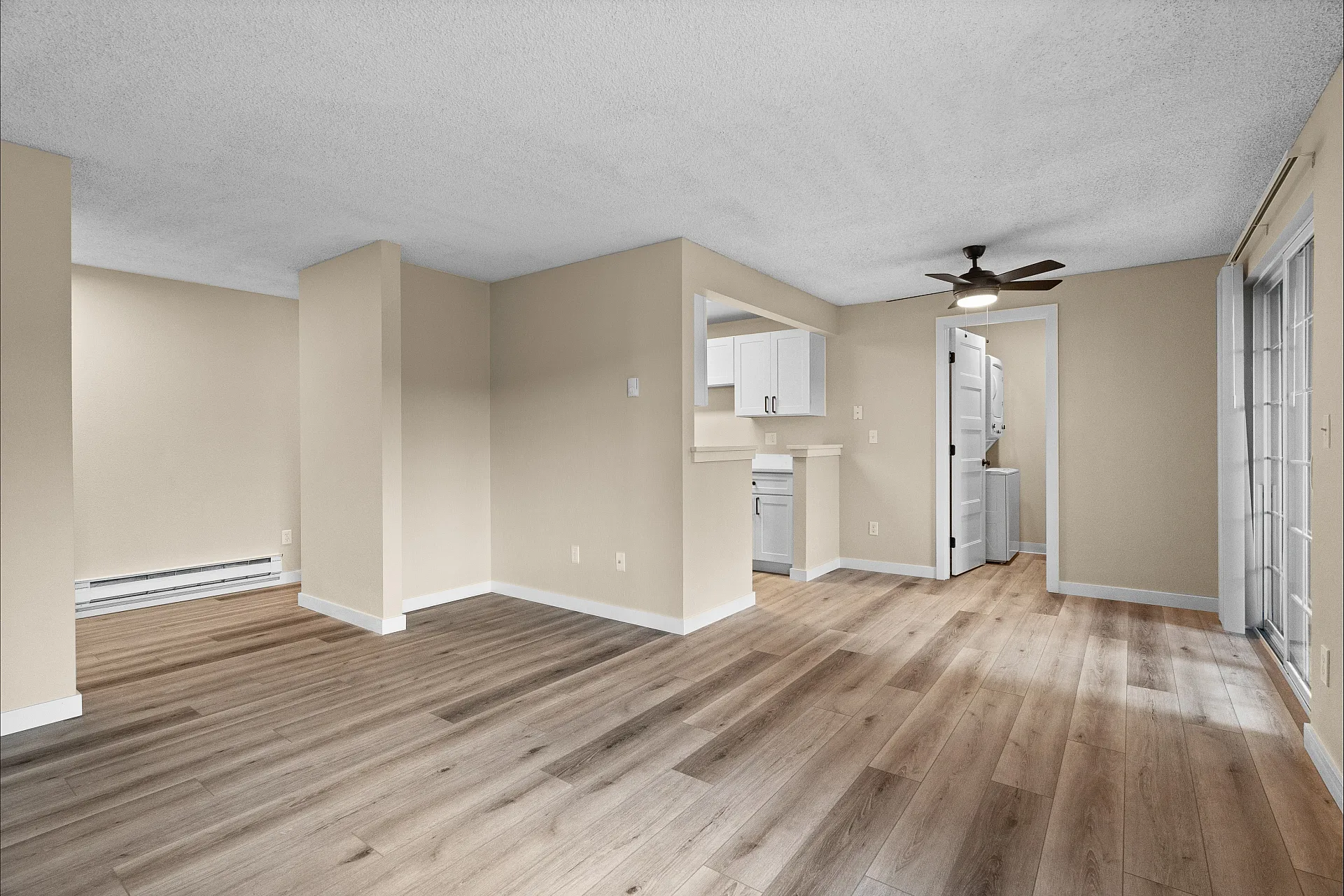 Bright, open-concept living area with elegant wooden flooring, sleek kitchen, and stylish ceiling fan, perfect for modern living.