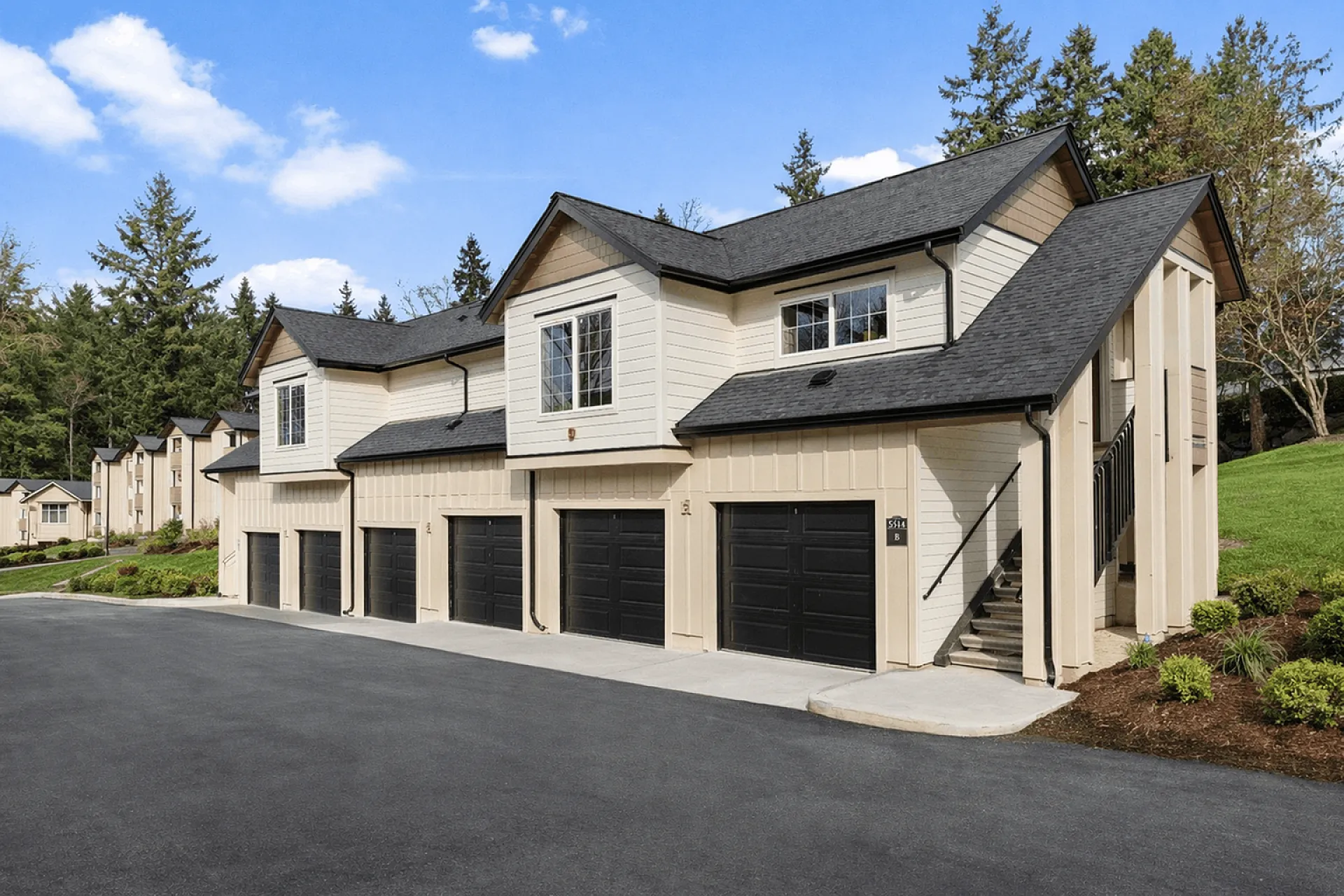 Charming townhomes with modern black garage doors, set in a serene environment with lush greenery and bright blue skies.
