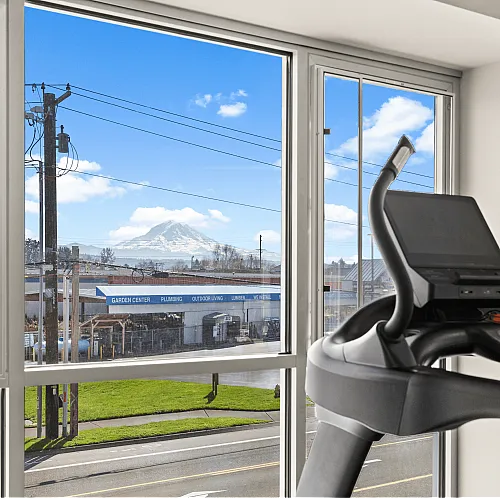 Bright gym space with a treadmill in front of a large window offering a stunning mountain view.