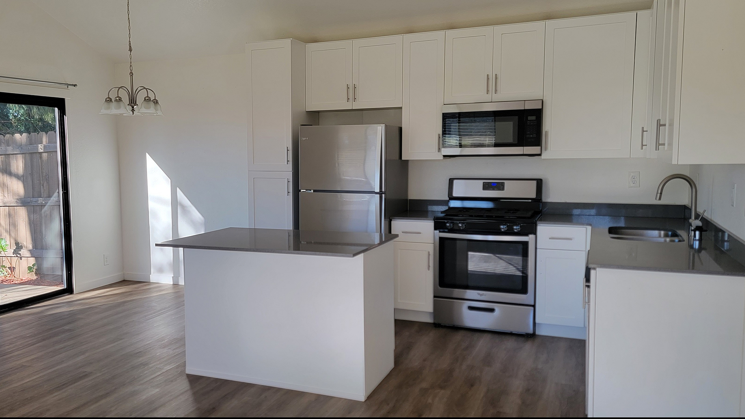 Bright and modern kitchen with sleek white cabinetry, stainless steel appliances, and a spacious island, enhanced by abundant natural light from large sliding doors leading to a serene outdoor area.