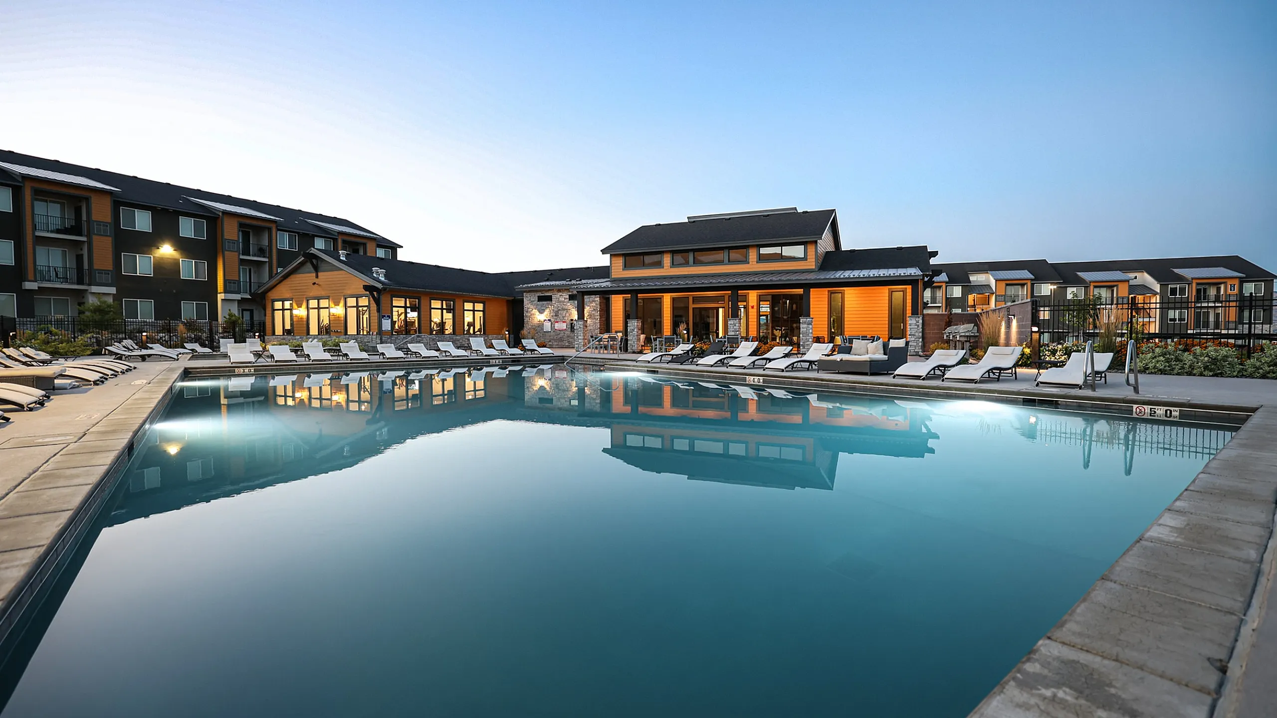 Luxurious apartment complex with a stunning outdoor pool and modern lounge chairs, surrounded by elegant architecture at sunset.