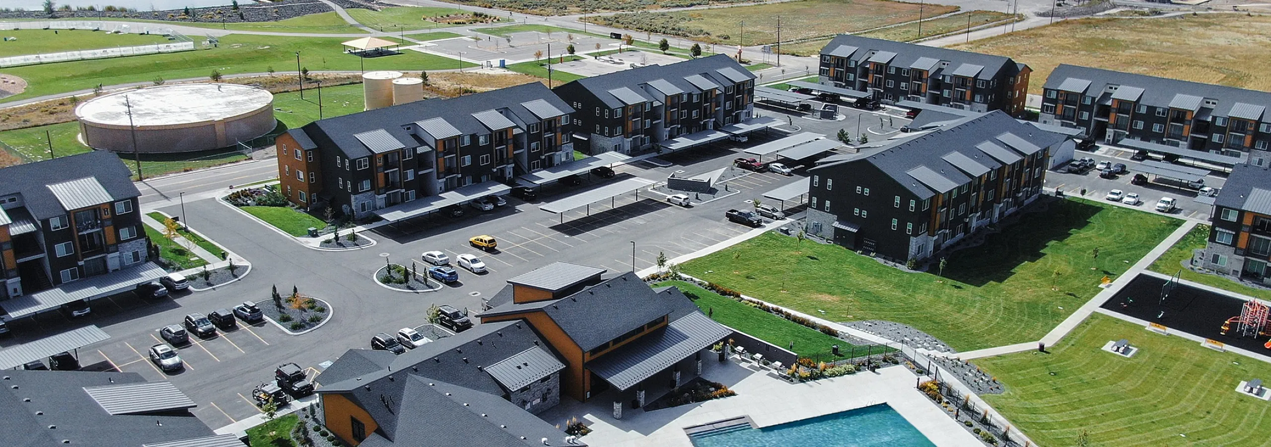 Scenic aerial view of a modern apartment complex with spacious pools, green landscaping, and mountain backdrop.