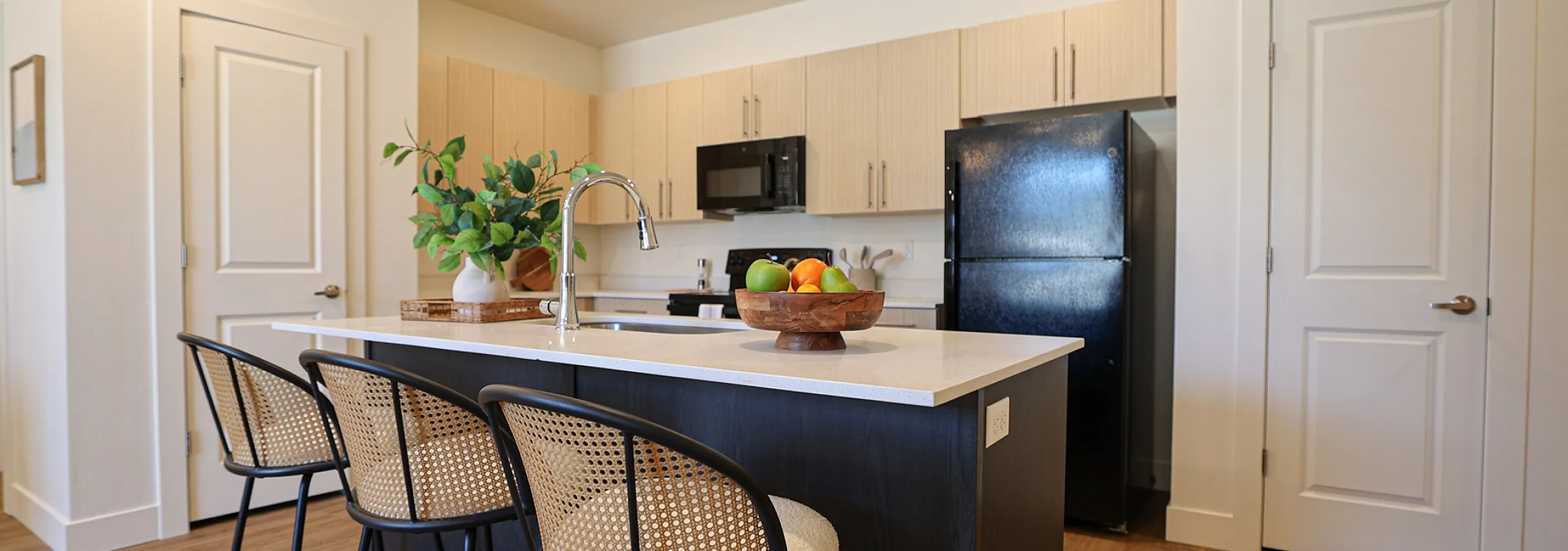 Contemporary kitchen with sleek black appliances, a stylish island with modern bar stools, and warm wooden flooring for a cozy ambiance.