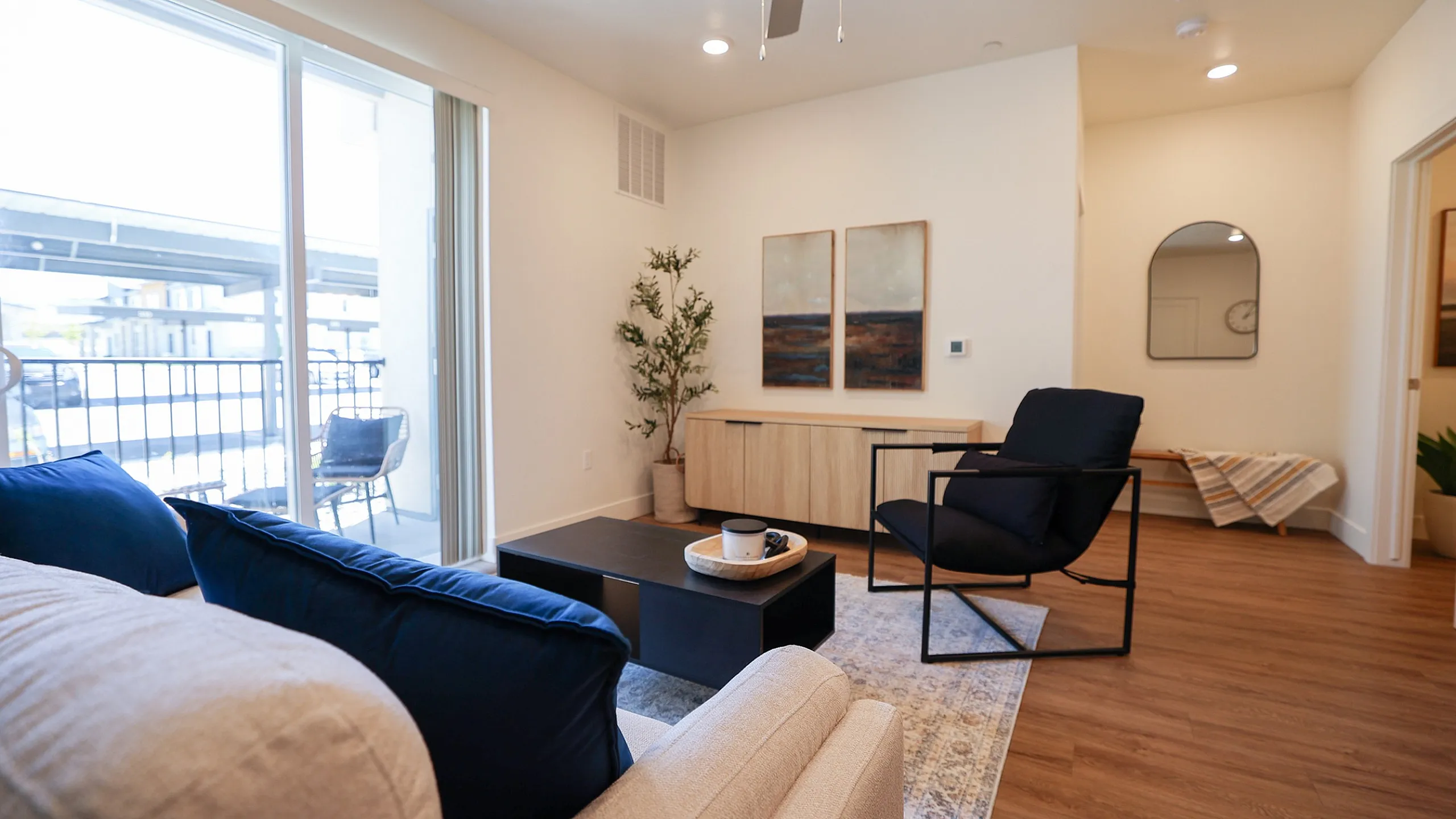 Bright and inviting living room with modern decor, featuring a comfortable sofa, sleek black chair, and large sliding glass door leading to a private balcony.