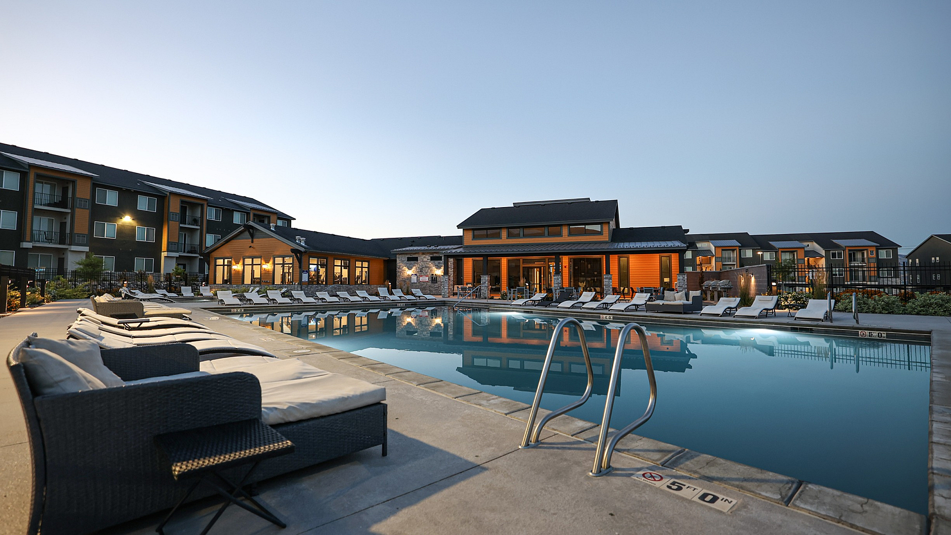 Elegant apartment complex showcasing a luxurious pool area with comfortable lounge chairs, modern architecture, and serene evening ambiance.