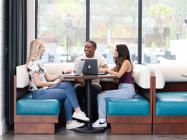 Bright and modern social space with young professionals collaborating at a cozy booth, featuring large windows and stylish seating.