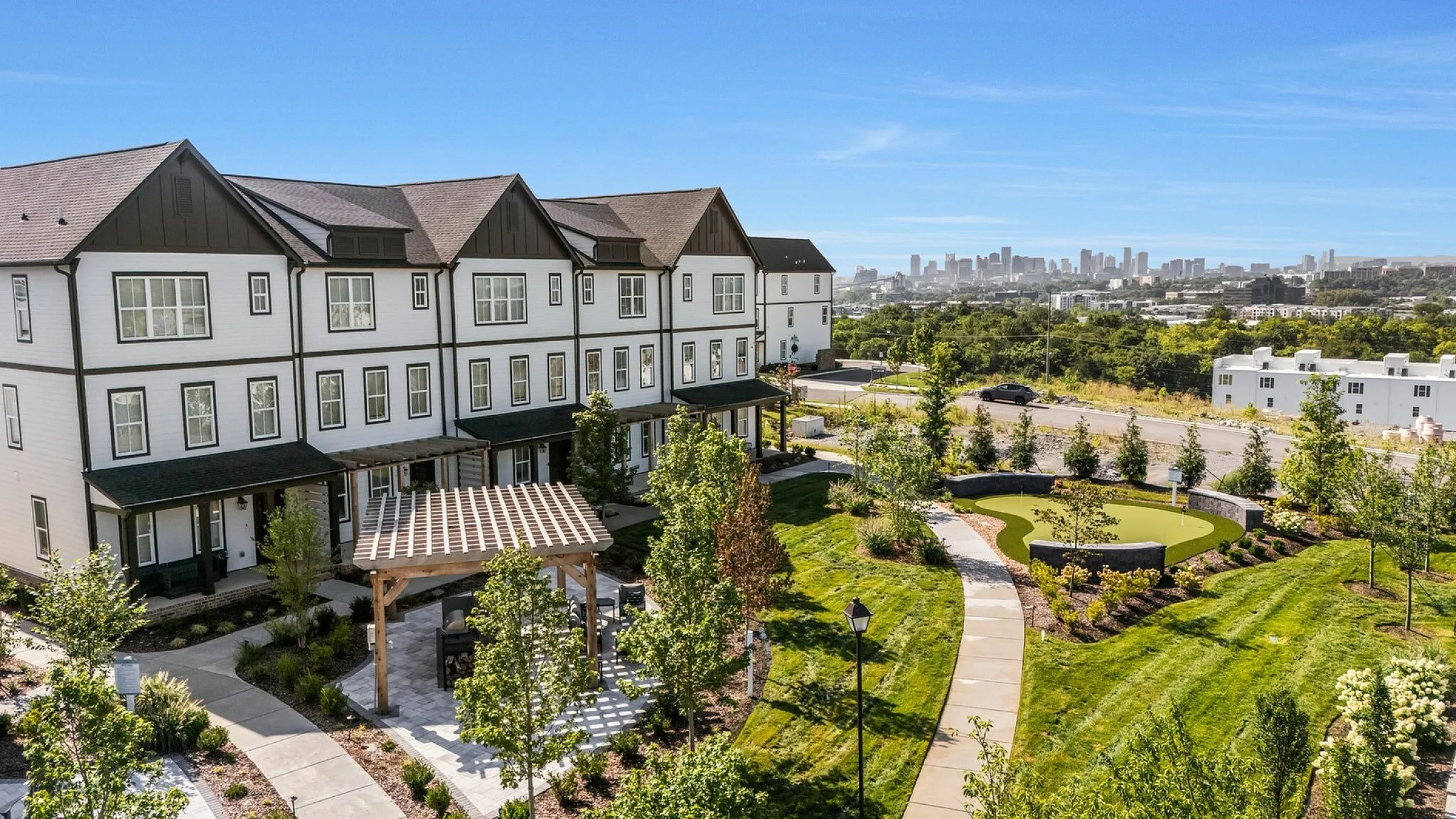 Charming townhouse complex with lush landscaping, pergola, and stunning cityscape views.