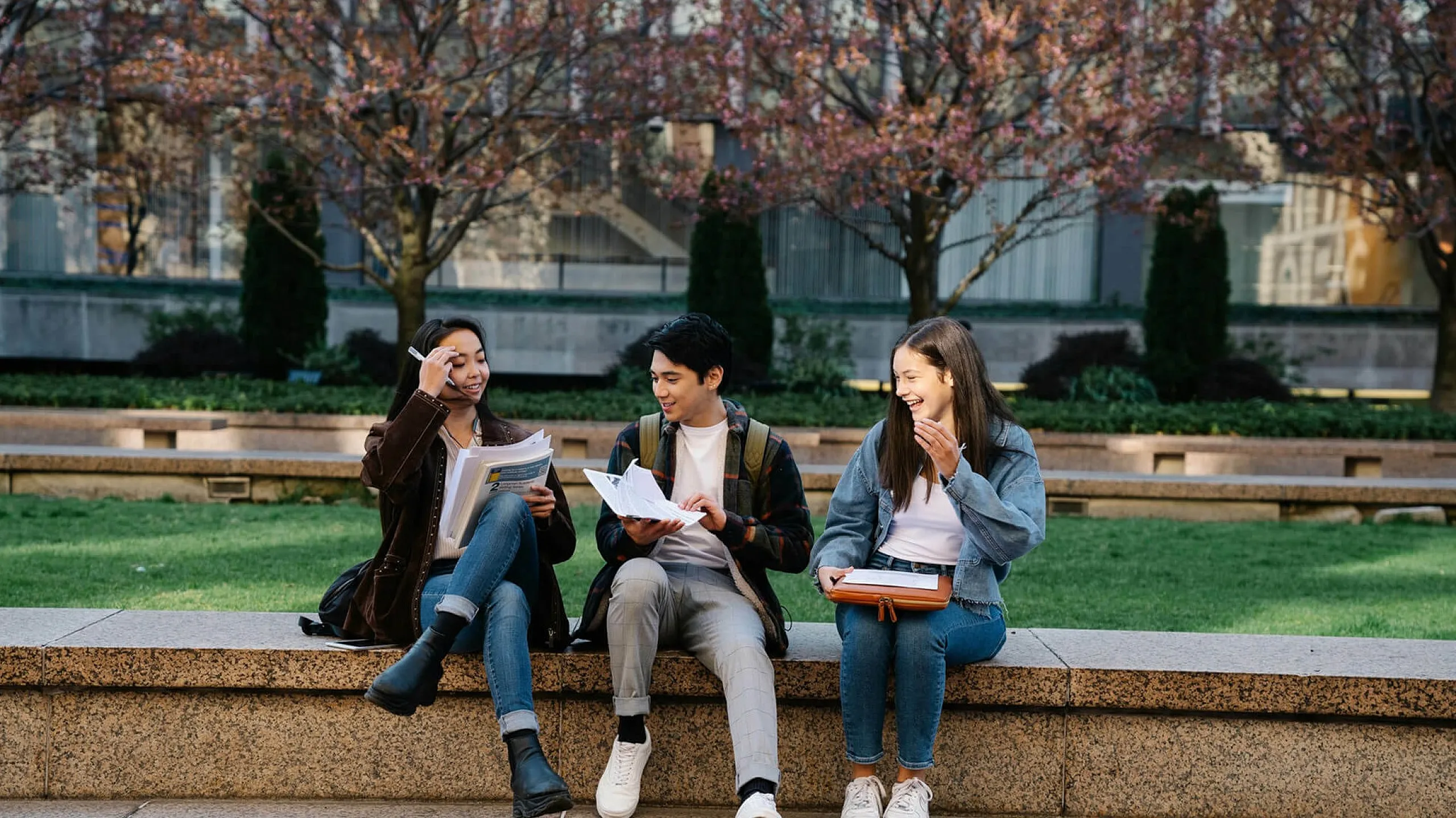 Three friends enjoying a lively conversation while sitting on a beautiful stone bench in a blooming garden, creating a vibrant and cheerful atmosphere.
