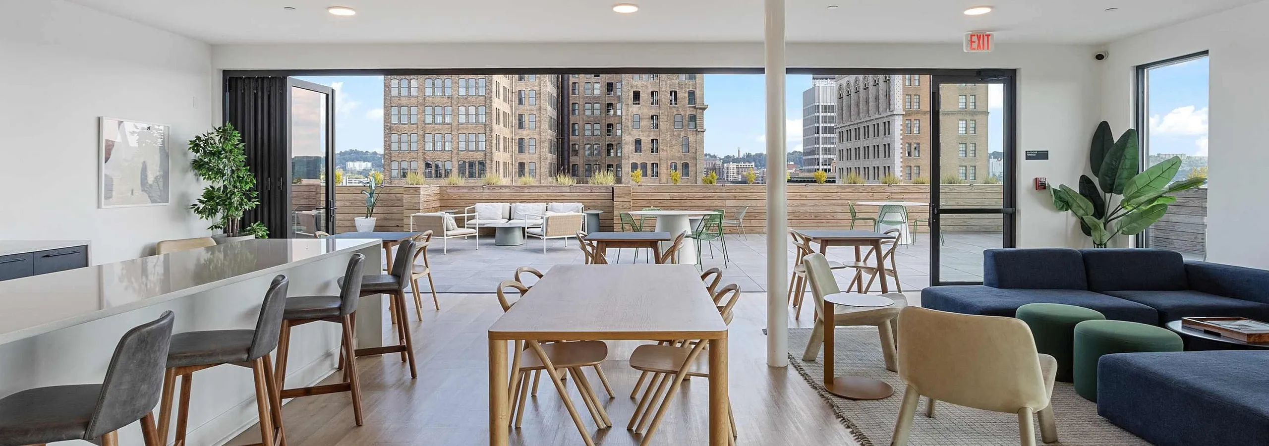 Bright and spacious open-concept living area featuring a sleek kitchen island, contemporary furnishings, and floor-to-ceiling windows with cityscape views, opening to a stylish outdoor terrace.