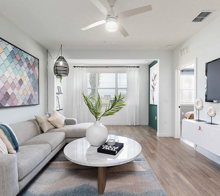 Bright and modern living room showcasing a cozy gray sofa, elegant wall art, and a sleek marble coffee table with vibrant decor, accentuated by large windows and stylish wood flooring.
