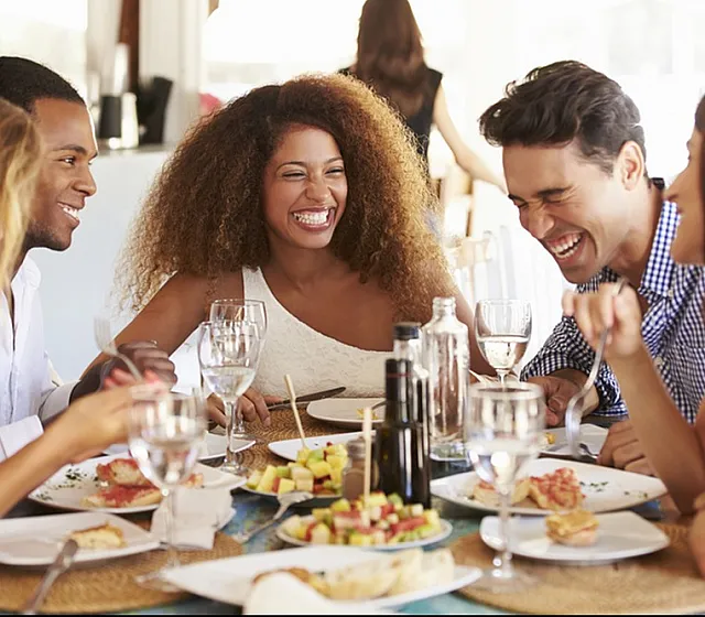 Joyful gathering of friends enjoying a meal at a bright and inviting dining area, showcasing a vibrant and social atmosphere.