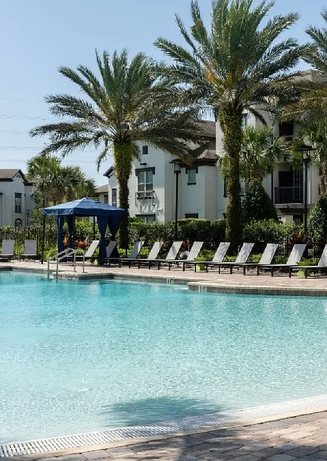Luxurious poolside view with palm trees and modern apartment homes, creating a resort-like atmosphere.