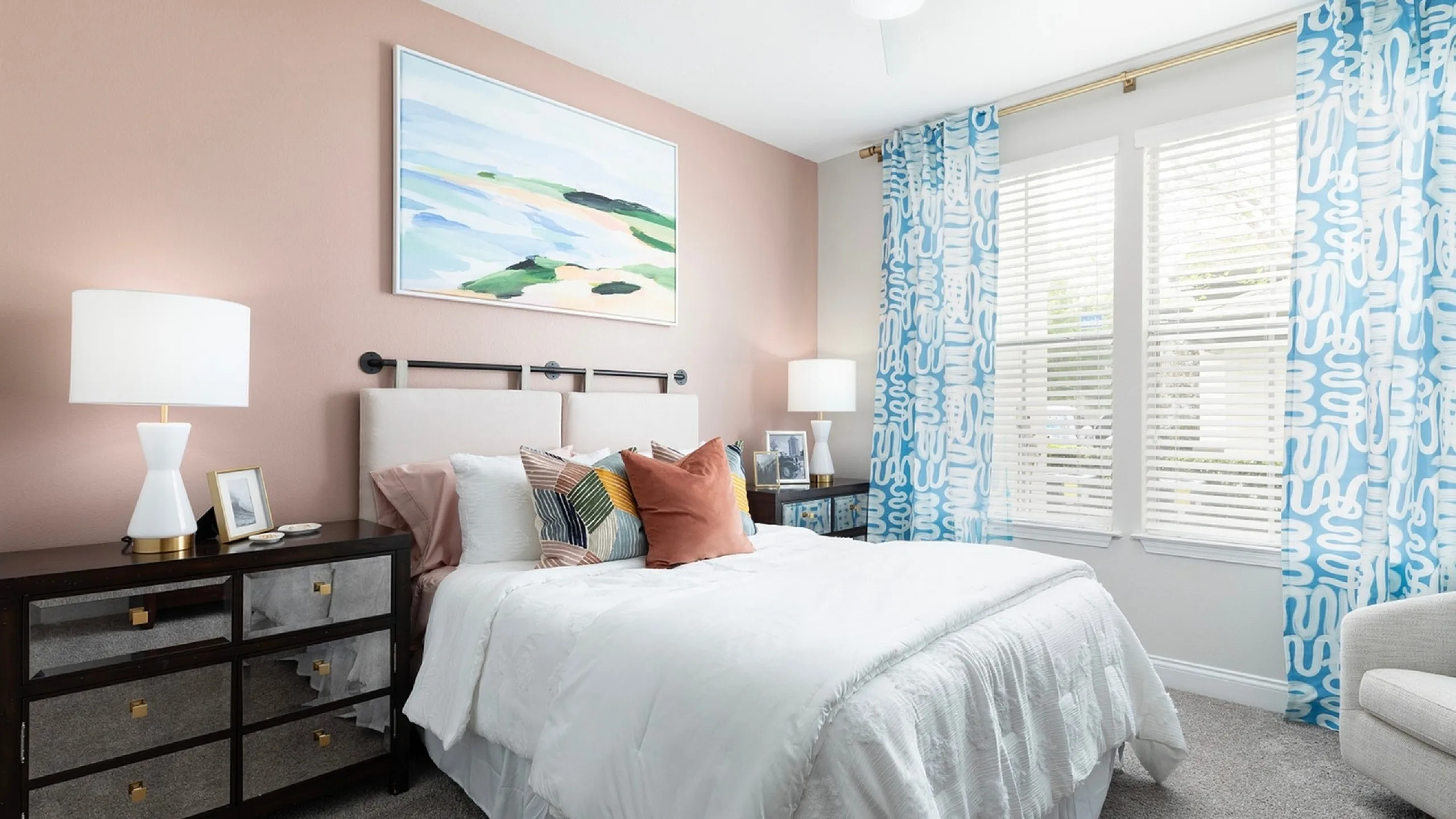 Charming bedroom with pastel accents, featuring a comfortable bed with colorful pillows, stylish bedside lamps, and bright natural light through patterned curtains.