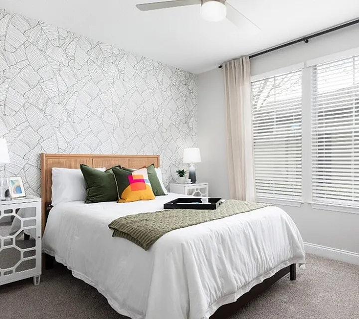 Bright and cozy bedroom with elegant wallpaper, plush decor pillows, and large windows offering abundant natural light.