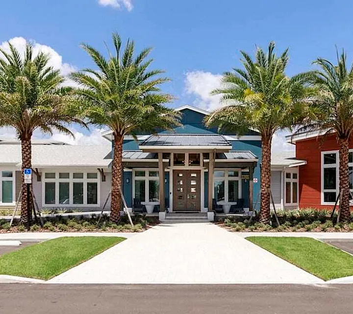 Modern community center with striking architectural design, surrounded by palm trees and lush landscaping, under a clear blue sky.
