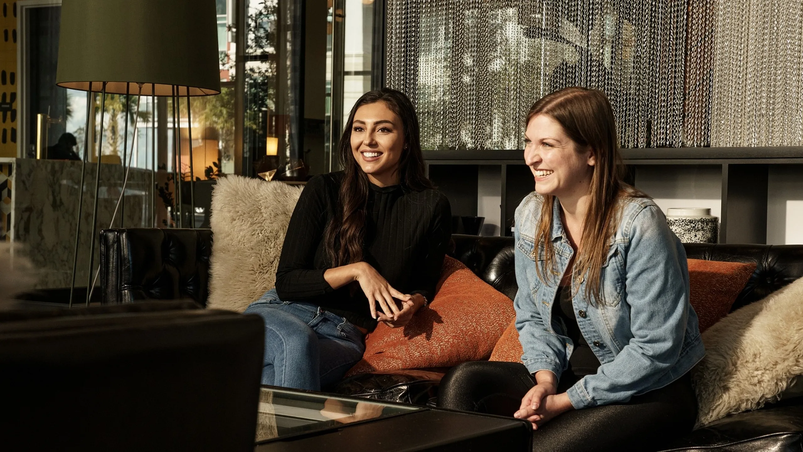 Inviting lounge area with two people enjoying a cozy conversation on a plush black sofa, complemented by stylish decor and warm lighting.