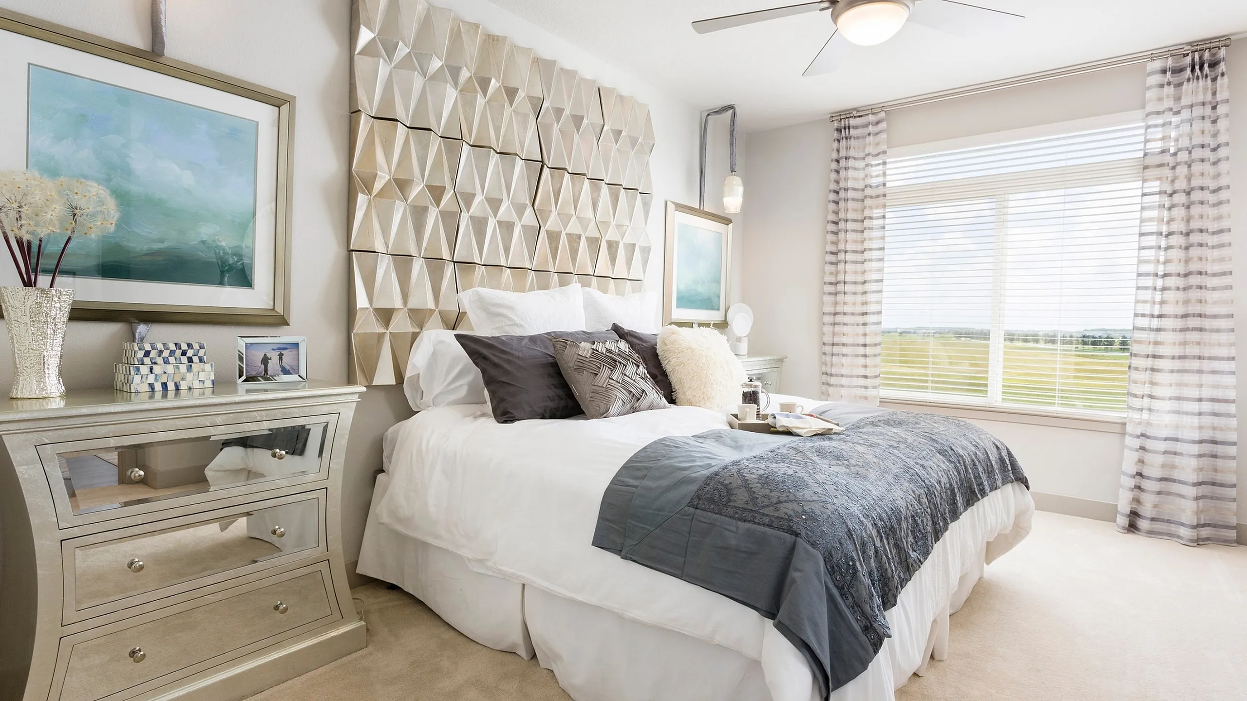 Bright and elegant bedroom with modern geometric wall art, stylish mirrored side table, and large window with scenic views.