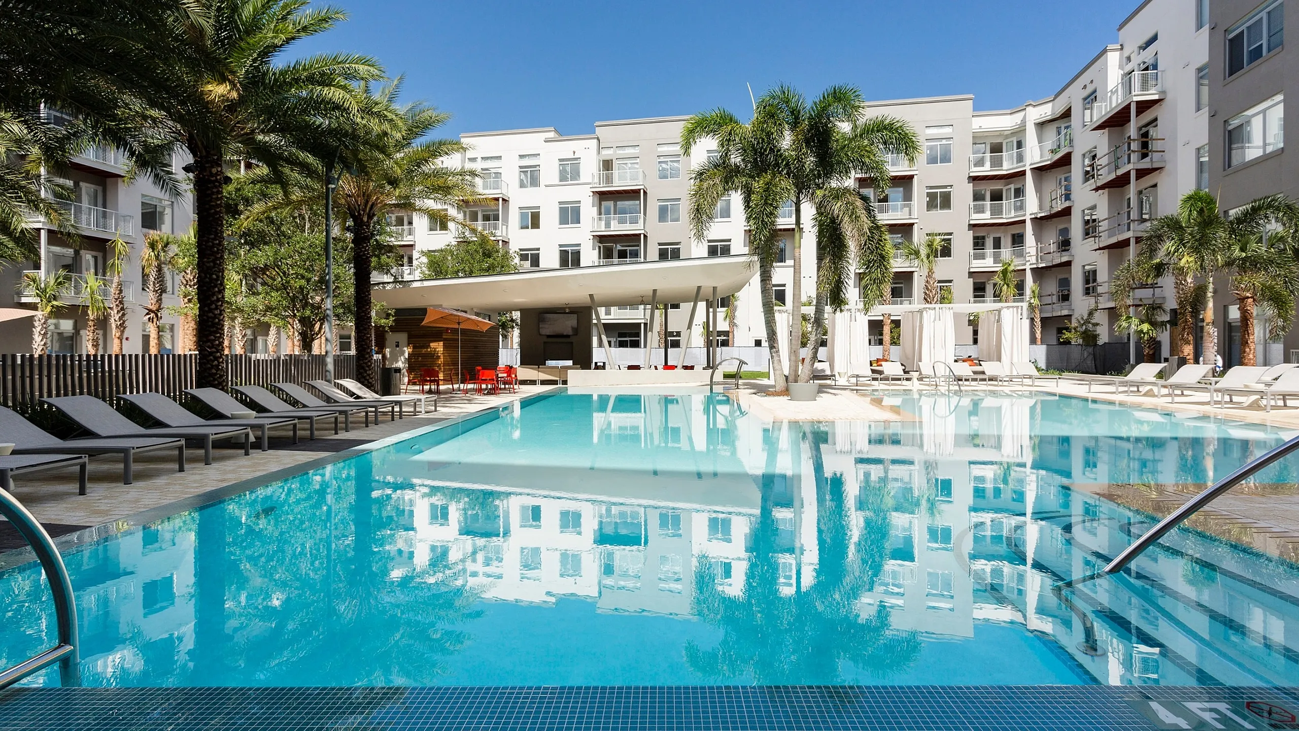 Luxurious apartment complex with a stunning outdoor pool surrounded by palm trees and modern architecture.