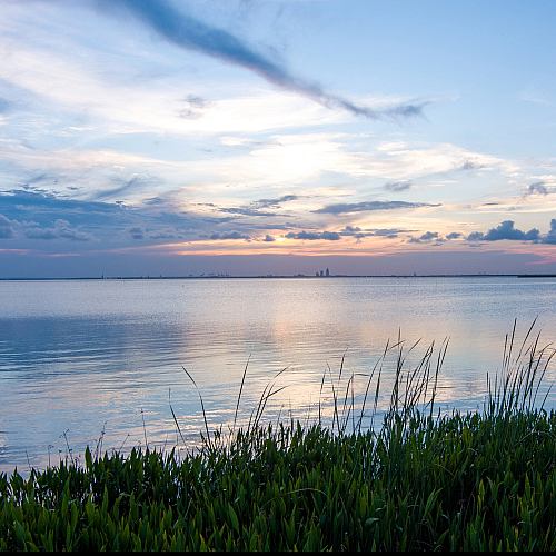 Serene lakeside view at dusk with colorful sky reflections and lush greenery in the foreground.