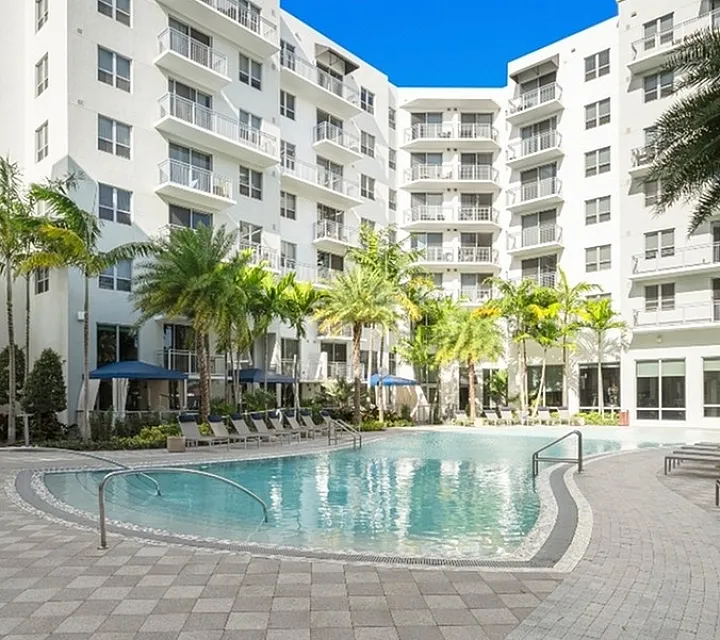Modern apartment complex with a luxurious pool surrounded by lush palm trees and stylish loungers.