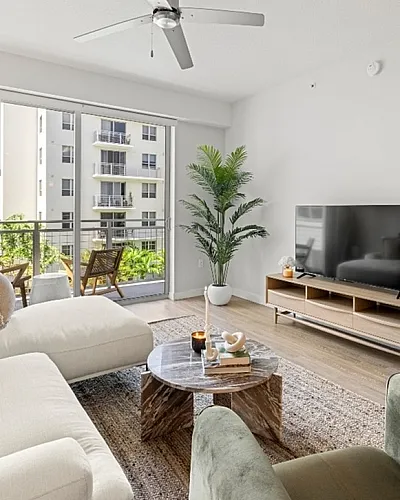 Chic, modern living room with natural light, featuring a plush white sofa, stylish decor, and a large flat-screen TV.