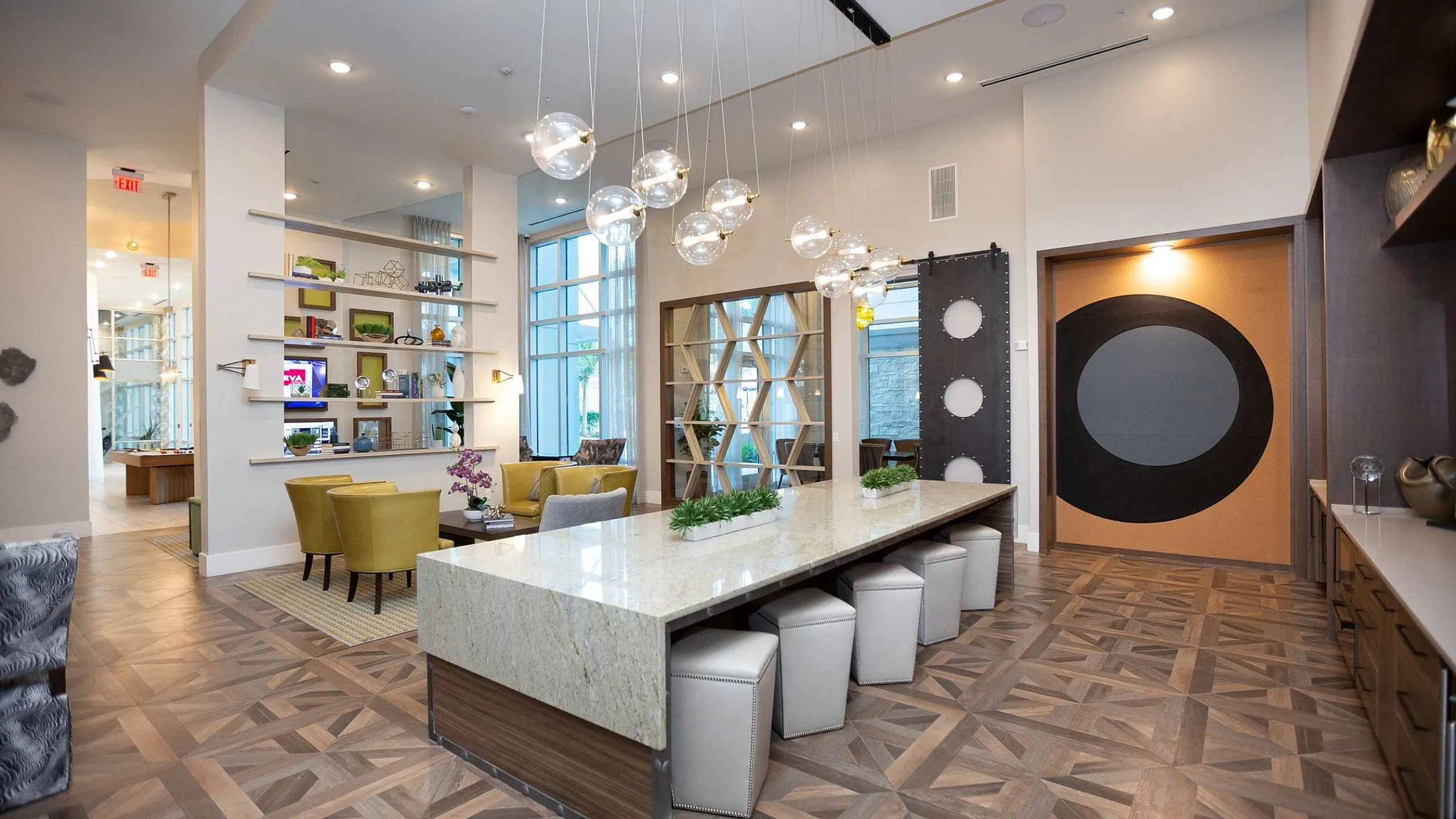Elegant modern apartment lobby showcasing a stylish design with a large granite-topped table, plush seating area, geometric floor patterns, and artistic shelving for a luxurious ambiance.