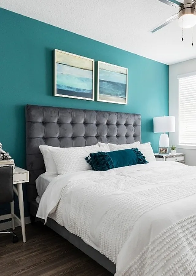Chic bedroom with teal accent wall, plush gray headboard, stylish desk, and modern decor.