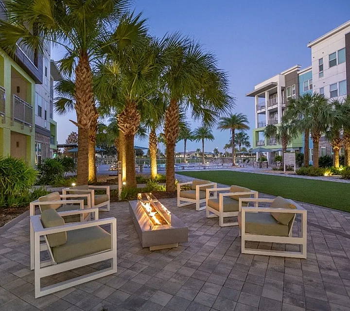 Chic outdoor seating area with modern fire pit surrounded by palm trees, perfect for relaxing evenings in a beautiful apartment complex.