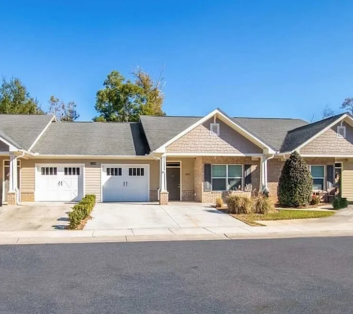 Charming duplex townhome with a welcoming driveway and lush landscaping in a serene neighborhood.
