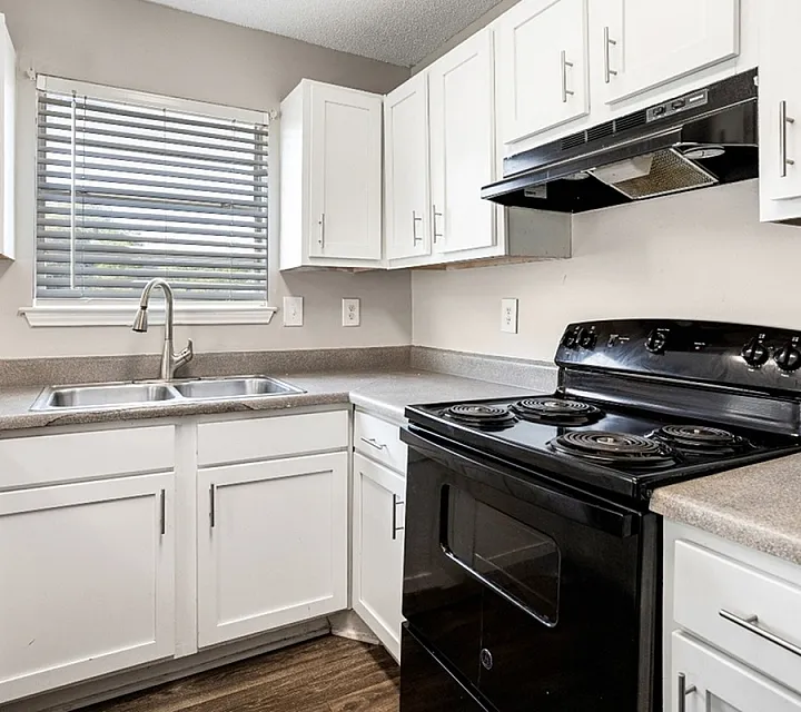 Charming kitchen with modern black appliances, sleek white cabinets, and inviting natural light from a large window.