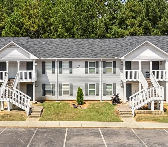 Charming two-story apartment building with inviting double staircases, nestled in a serene wooded area.