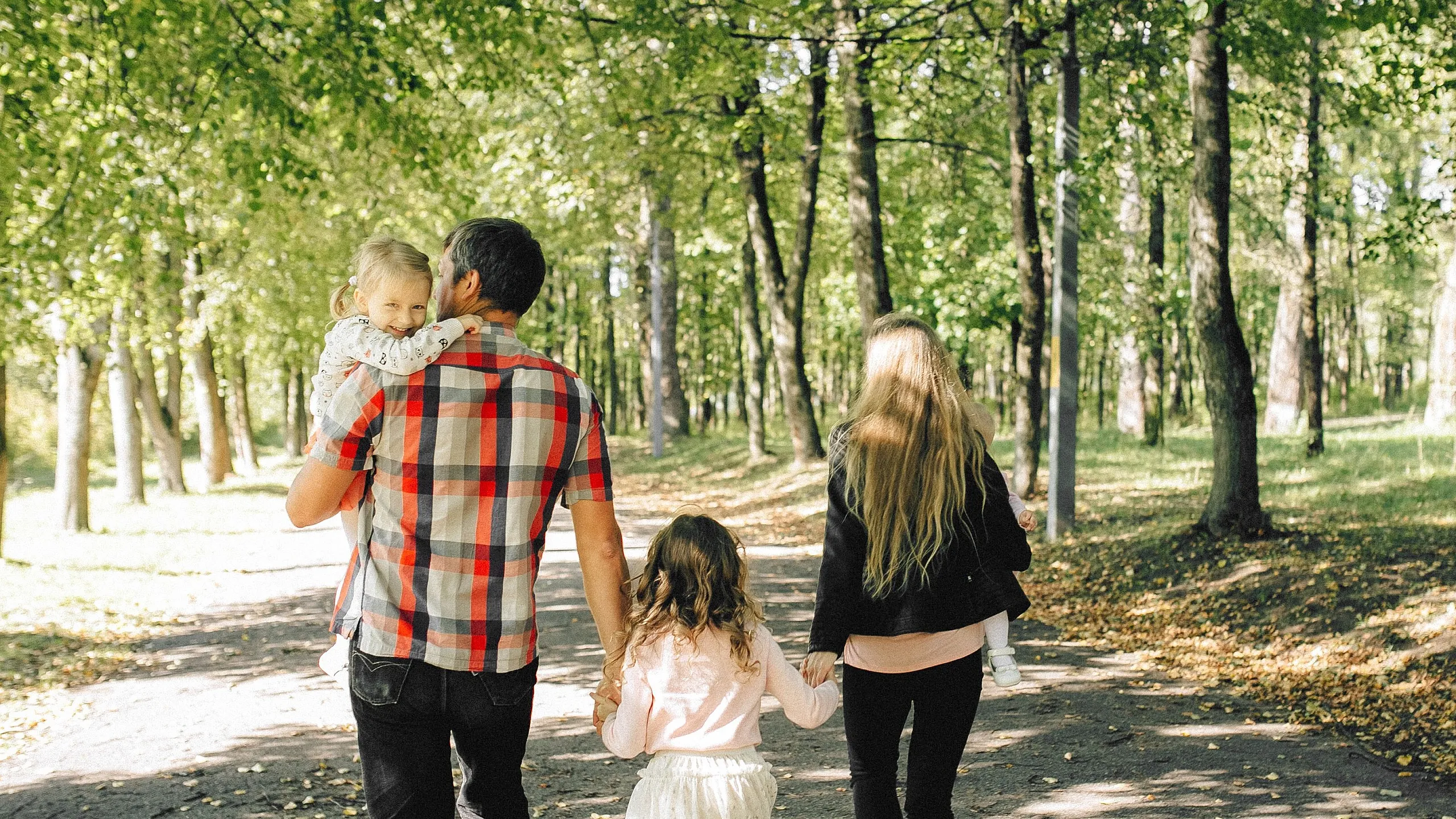 Family enjoying a peaceful walk in a sunlit park, surrounded by lush green trees.