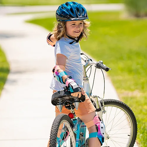 Joyful child cycling on a sunny path, wearing colorful protective gear and a helmet, surrounded by vibrant green grass.