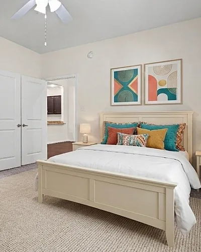 Elegant bedroom with vibrant decor, featuring a cozy bed, modern art, and soft lighting, connected to an en-suite bathroom and hallway.