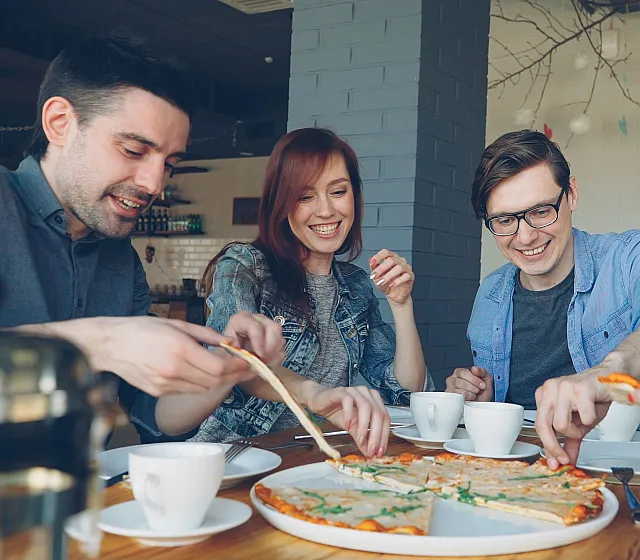 Vibrant group of friends enjoying pizza and coffee in a modern and cozy dining space.