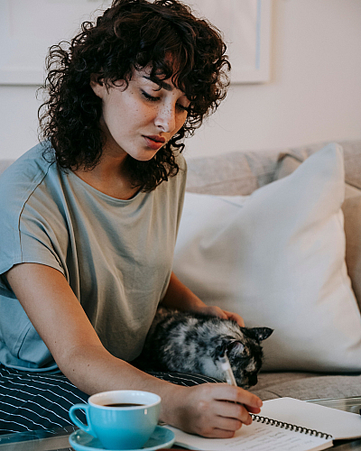 Cozy living space with a person writing in a notebook, relaxing next to a content cat on a comfortable couch.