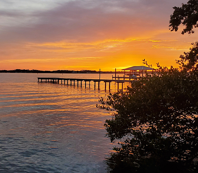 Breathtaking sunset view over a serene waterfront with a scenic pier and vibrant orange sky.