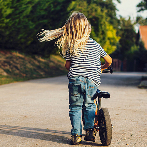 Child joyfully riding a bicycle on a sunny path surrounded by lush greenery.