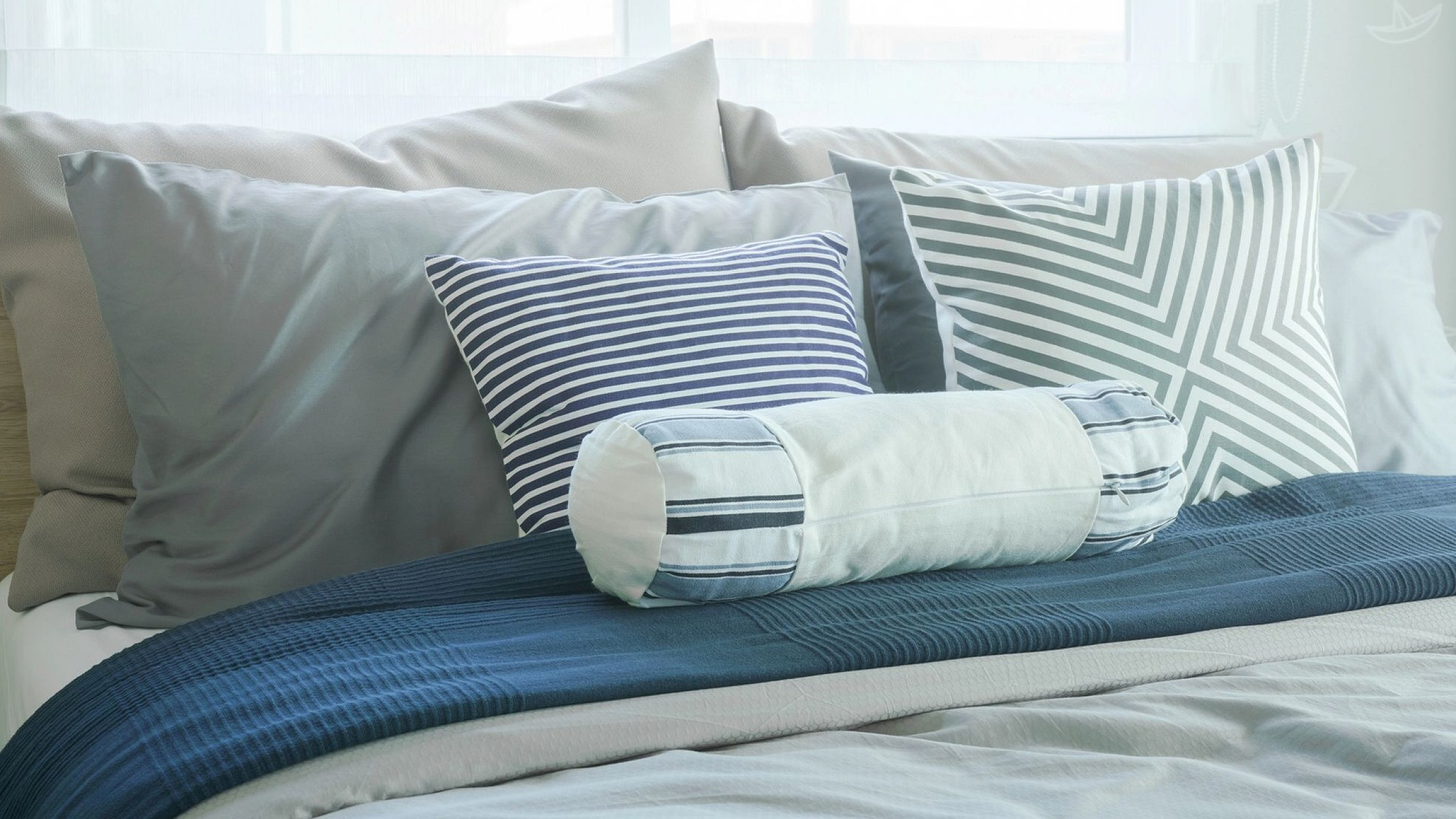 Luxurious bed setup with elegant striped pillows and a textured navy throw, creating a cozy and stylish bedroom ambiance.