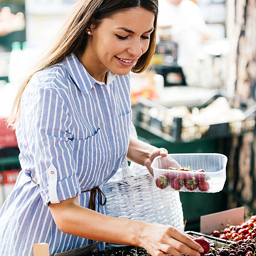 Vibrant farmers market scene with a woman selecting fresh strawberries and cherries, showcasing a lively shopping experience.