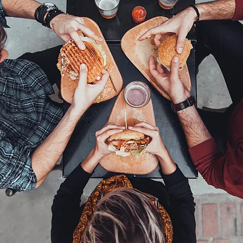 Top view of friends enjoying gourmet burgers and drinks at a cozy outdoor setting, highlighting a casual dining experience.