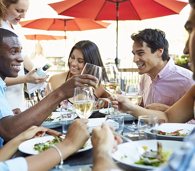 Lively outdoor dining scene with friends enjoying wine and laughter under vibrant red umbrellas.