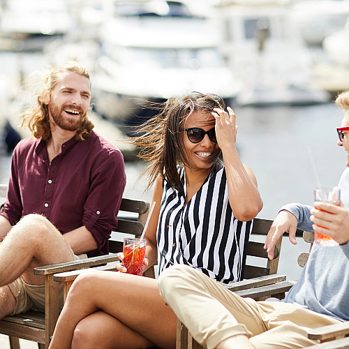 Vibrant group of friends enjoying drinks at a sunny marina, surrounded by luxury yachts and laughter.